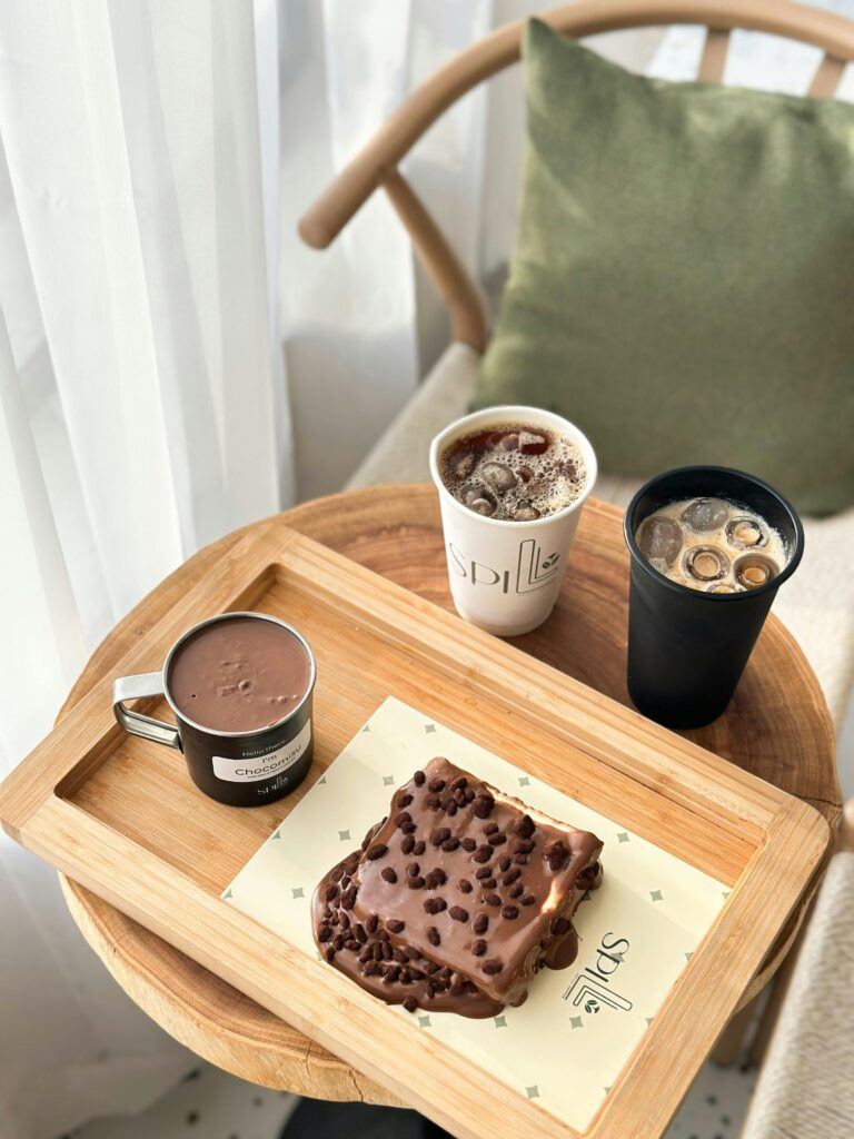 A cozy setting with coffee and desserts placed on a wooden tray by the window, suitable for cafes.