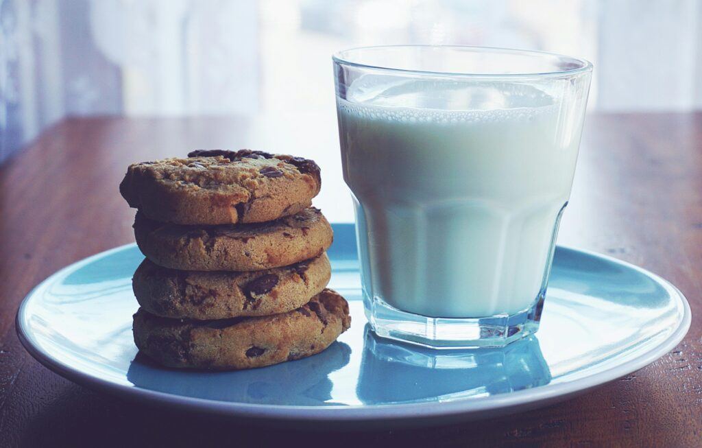 Close-up of chocolate chip cookies stacked beside a glass of milk on a blue plate.