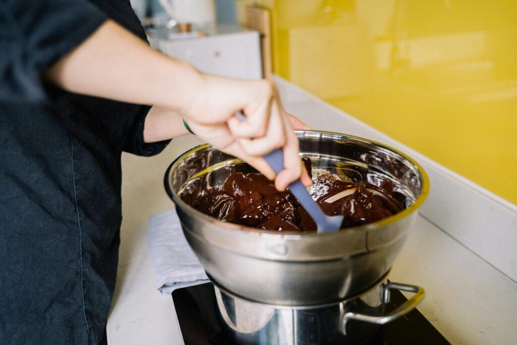 A person mixes rich melted chocolate in a stainless steel bowl for dessert preparation.